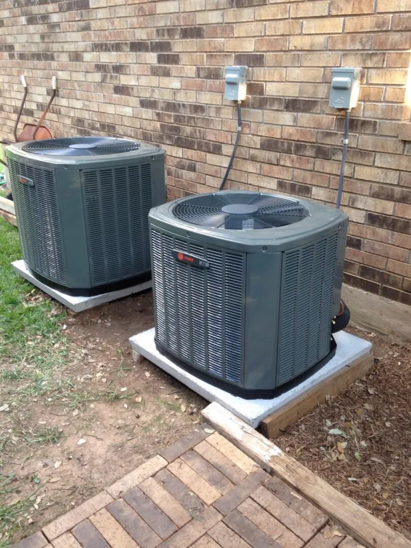 two air conditioner units outside of a brick house